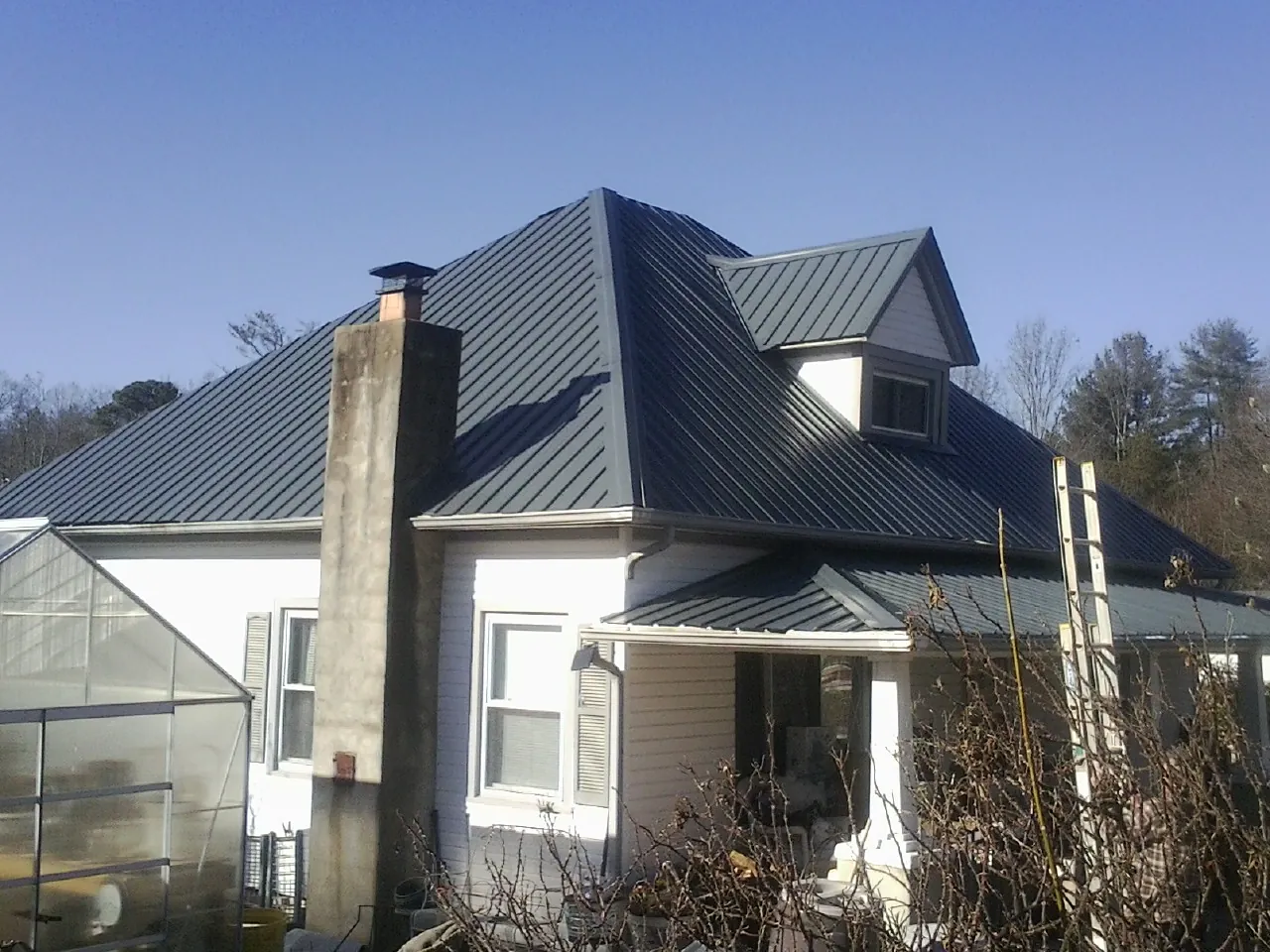 Dark blue standing seam metal roof on a white farmhouse with dormer — Slate & Tile Roof Repair by Roofing Brothers in Northpoint