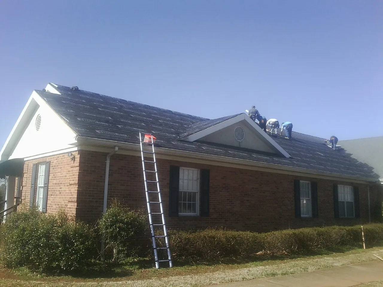 Crew tearing shingles off a brick ranch roof with a ladder set — Emergency Roof Repair work by our crew in Northpoint