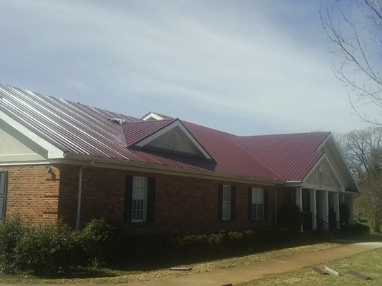Red metal roof with gabled entries on a long brick building, from a Hail Damage Roof Repair job in Northpoint
