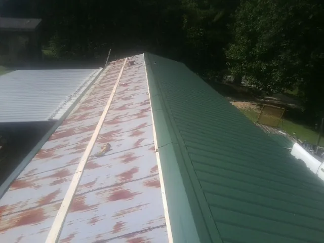 Old rusted panels beside newly installed green metal roofing — Wind Damage Roof Repair by Roofing Brothers in Northpoint