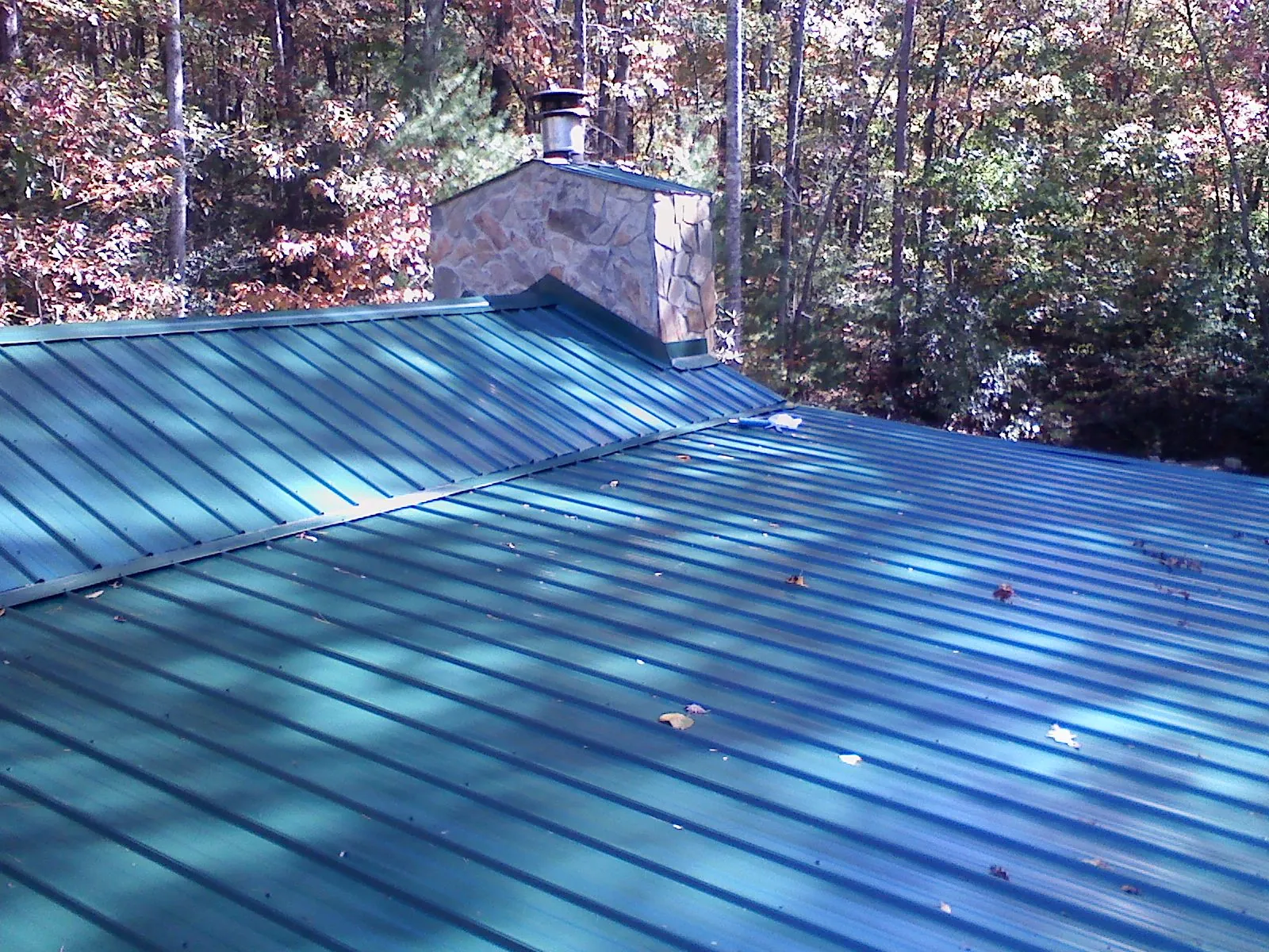 New green metal roof and stone chimney surrounded by autumn woods in Northpoint